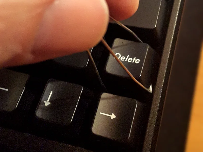 Wire keycap puller lifting a keycap straight up from a keyboard