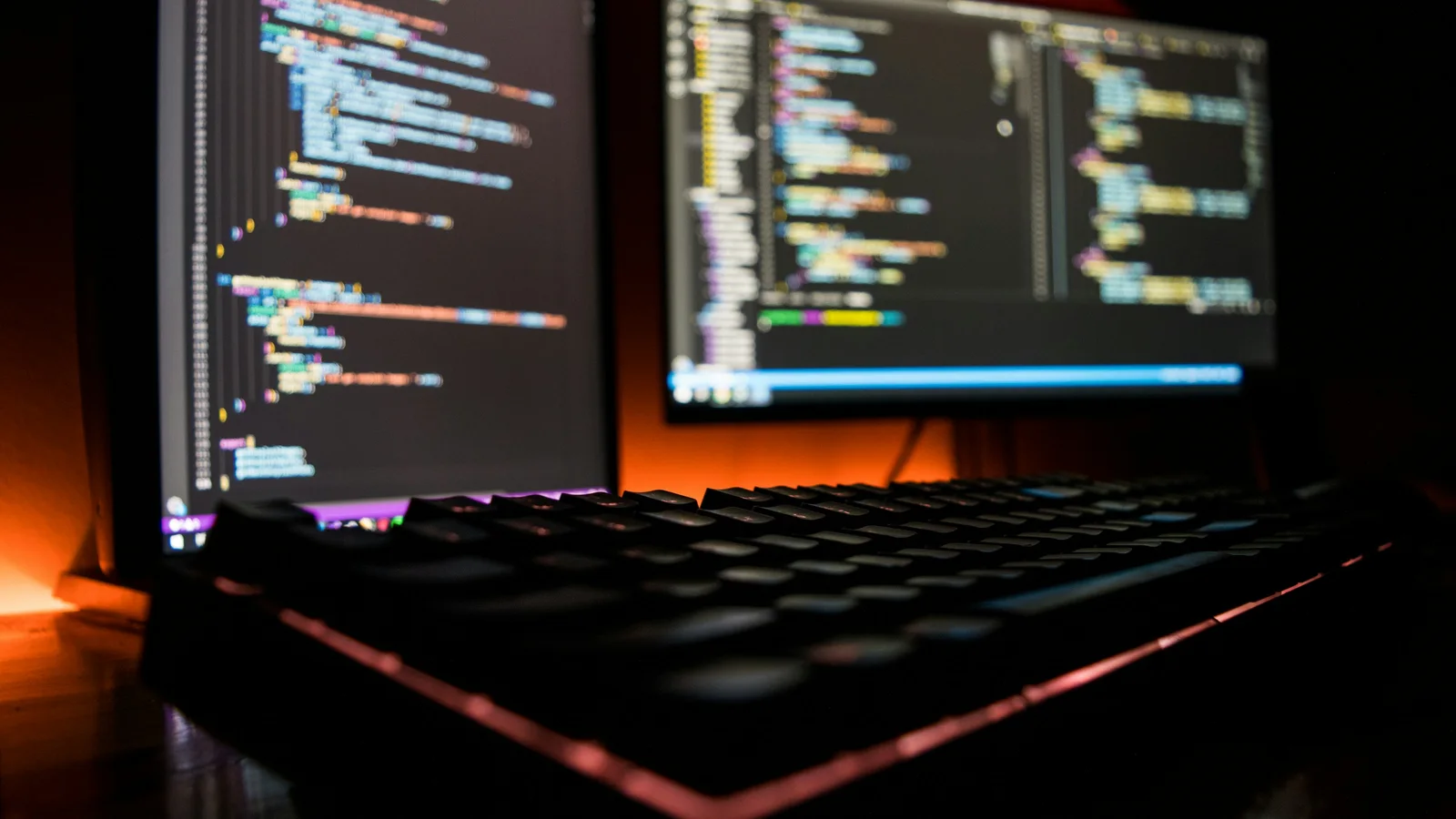 Mechanical keyboard in front of computer screens displaying source code