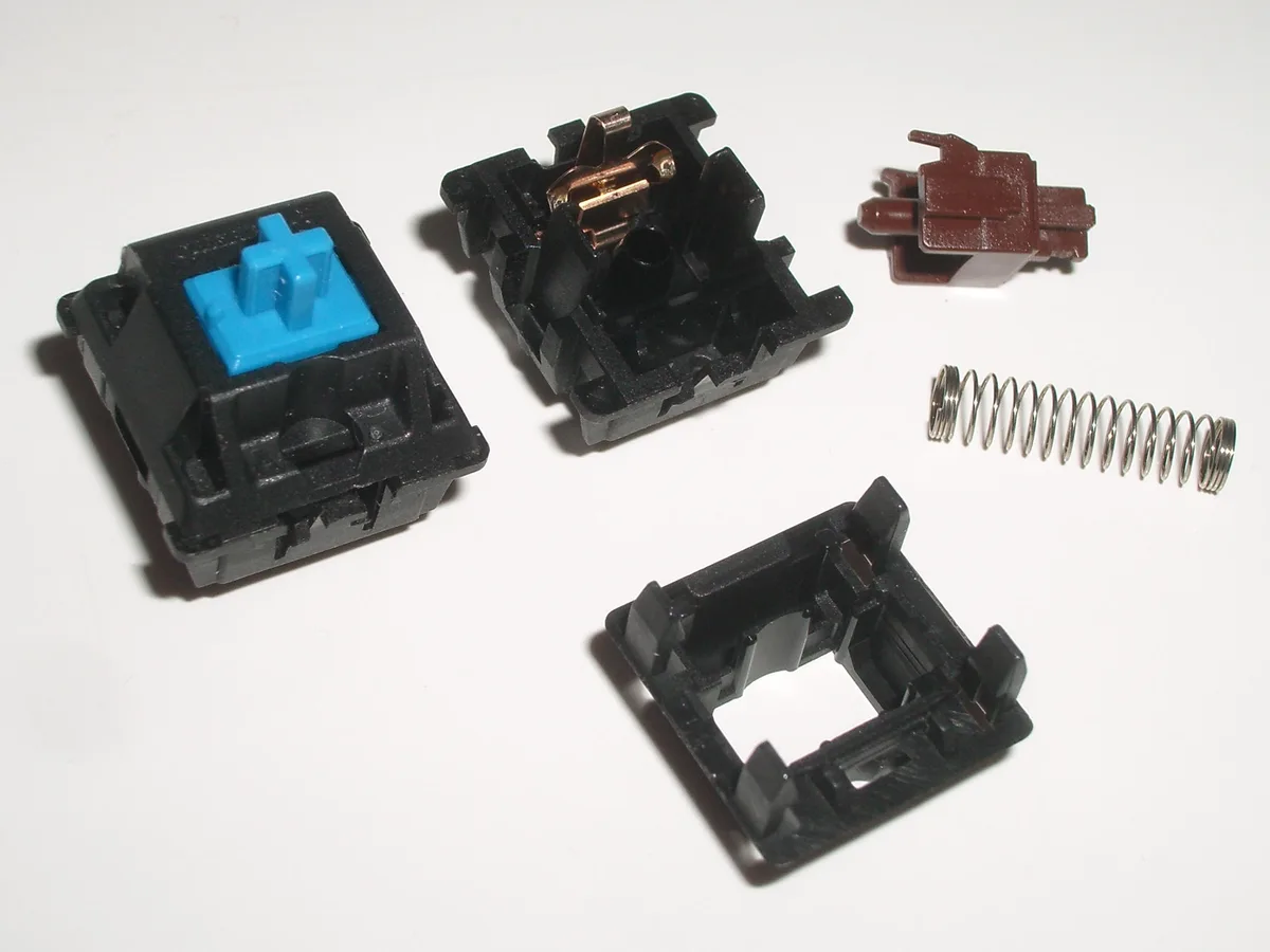 Disassembled tactile switch showing the stem profile, spring, contact leaf, and housing