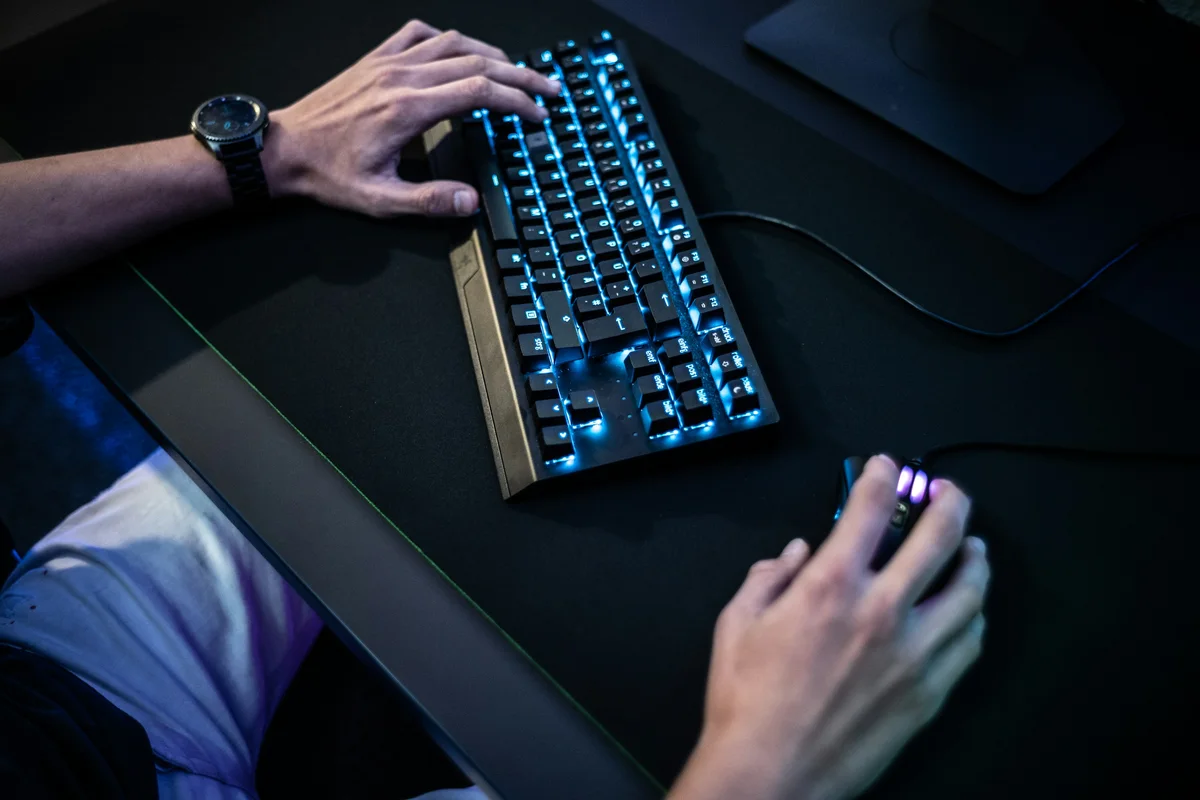 Person using a blue-backlit keyboard in a dim workspace