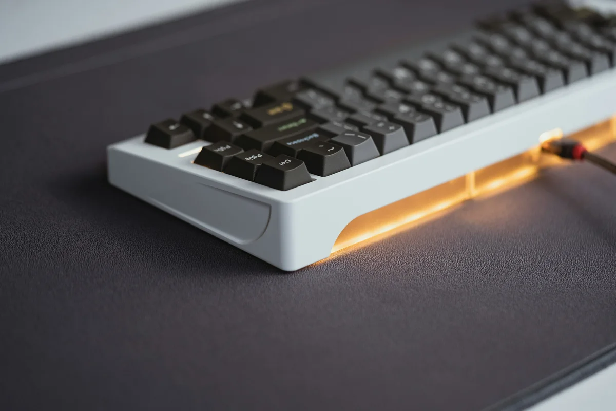 White mechanical keyboard with warm underglow illuminating the desk beneath its case