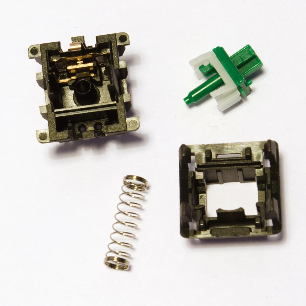 Disassembled mechanical switch showing the housing, stem, spring, and metal contacts