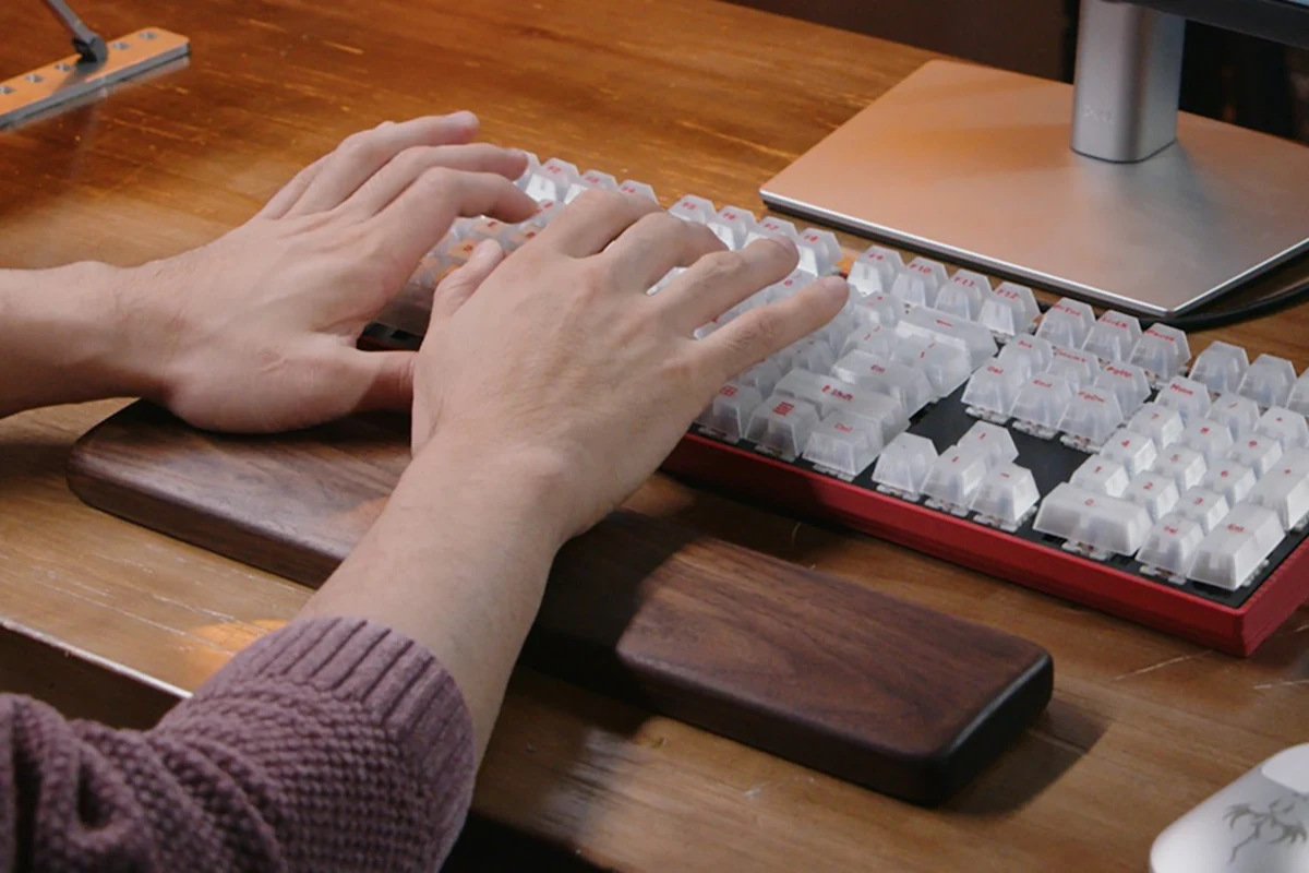 Hands typing on a mechanical keyboard with a wooden wrist rest